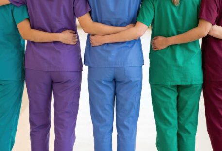Diverse group of female healthcare professionals standing together in a hospital hallway, arms around each other in a show of unity and support.